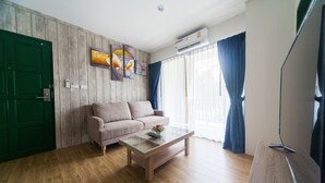 Una sala de estar con piso de madera, una puerta verde, un sofá color beige, una mesa de centro de vidrio y un televisor de pantalla plana.