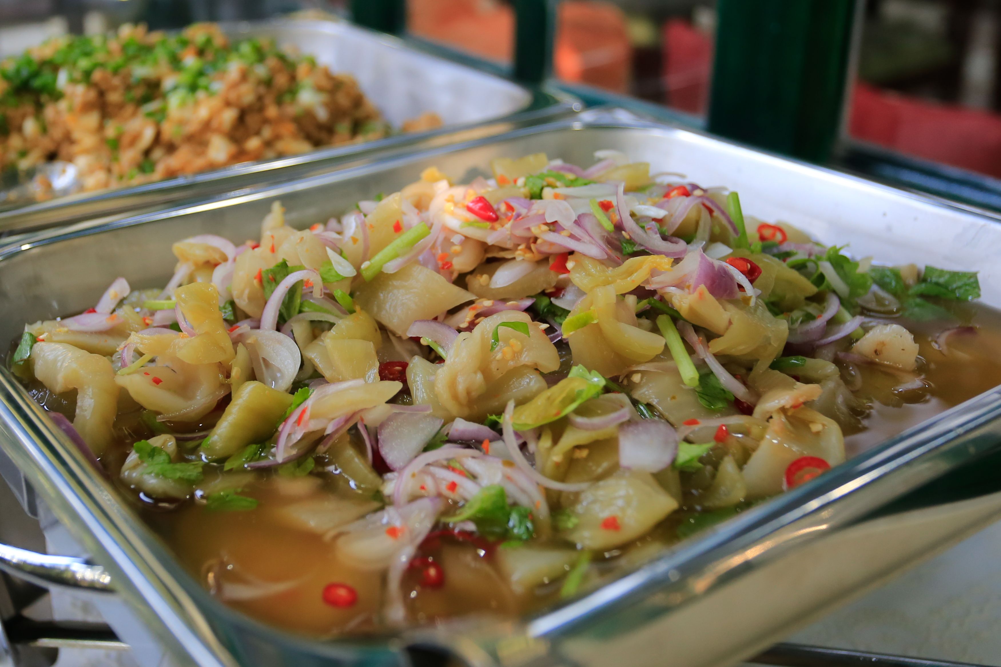 A buffet with various dishes, including a salad with vegetables and a dish with a red sauce.