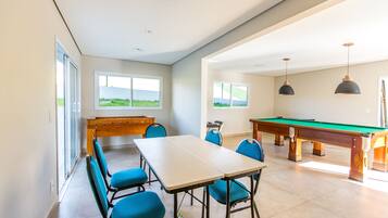 Una habitación amplia con mesa de billar, mesa de fútbol de mesa y mesa de billares. Hay cuatro sillas azules alrededor de una mesa rectangular.