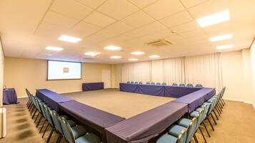 A conference room with a long table, chairs, a projector screen, and curtains.