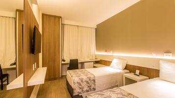 A hotel room with two beds, a desk, a chair, and a TV.