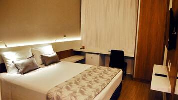A hotel room with a bed, bedside table, desk, and a television.