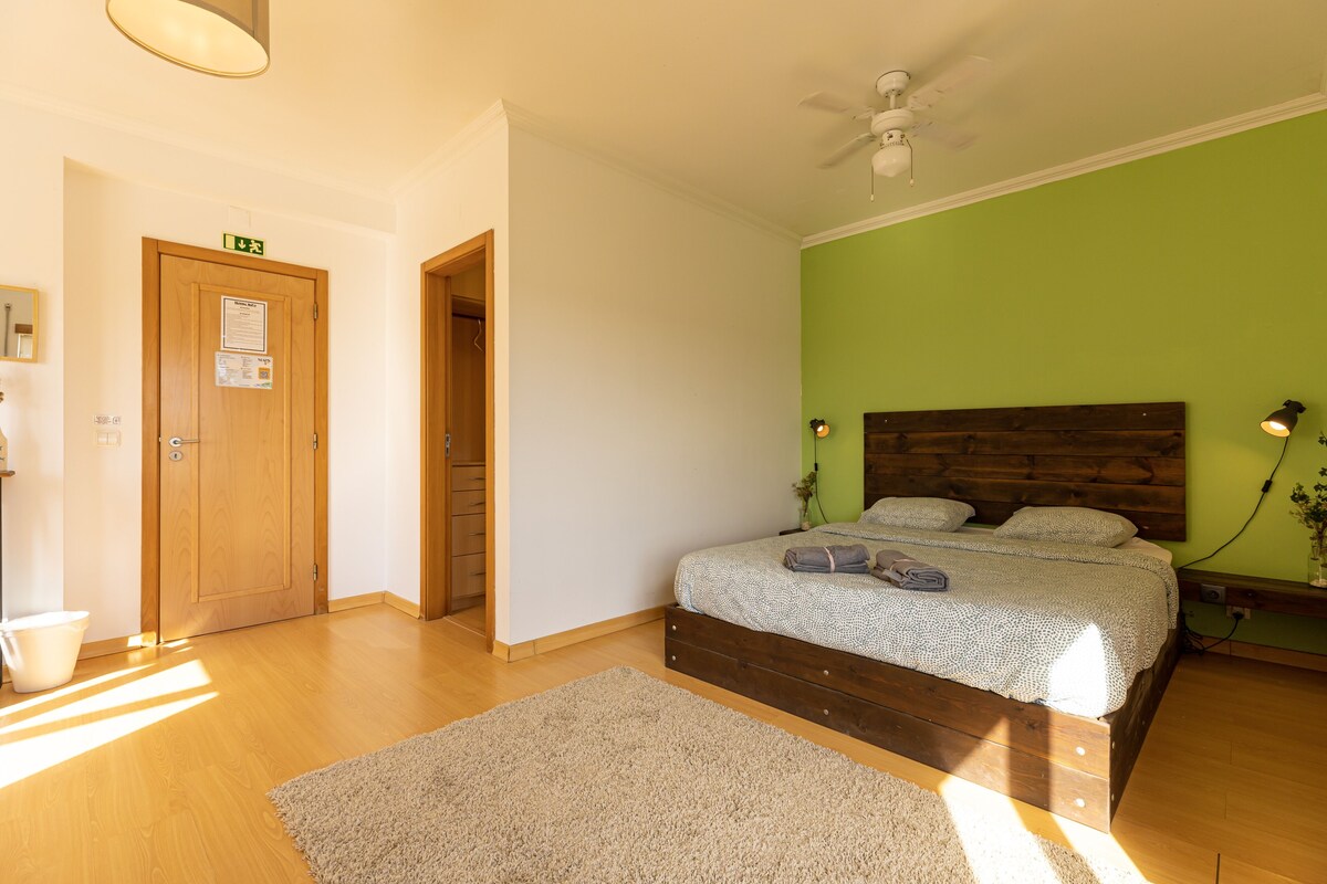A bedroom with a wooden bed, green walls, a ceiling fan, and a light fixture.