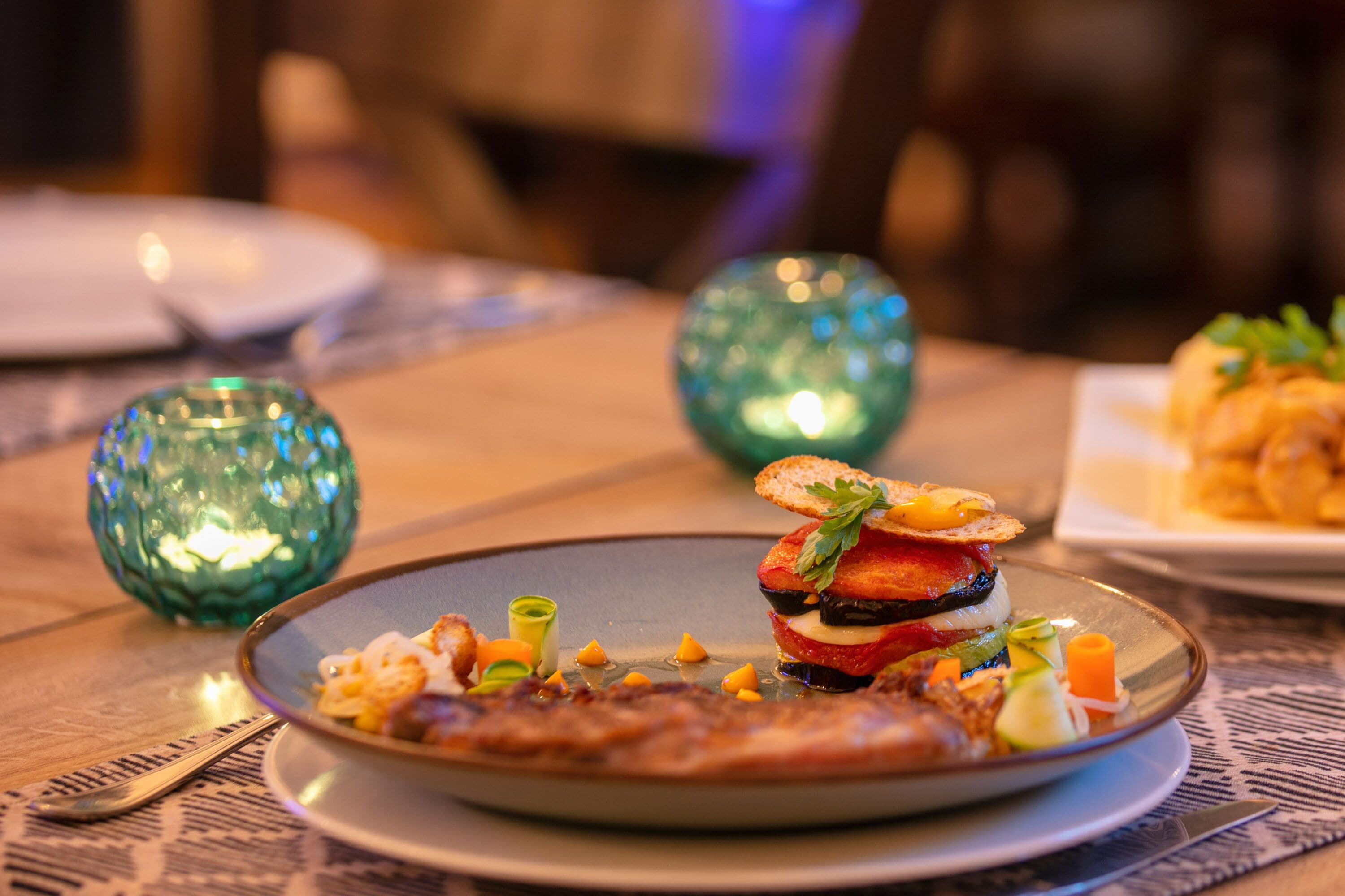 Una mesa de comedor con un plato de comida, una cuchara y dos jarrones de vidrio decorativos.