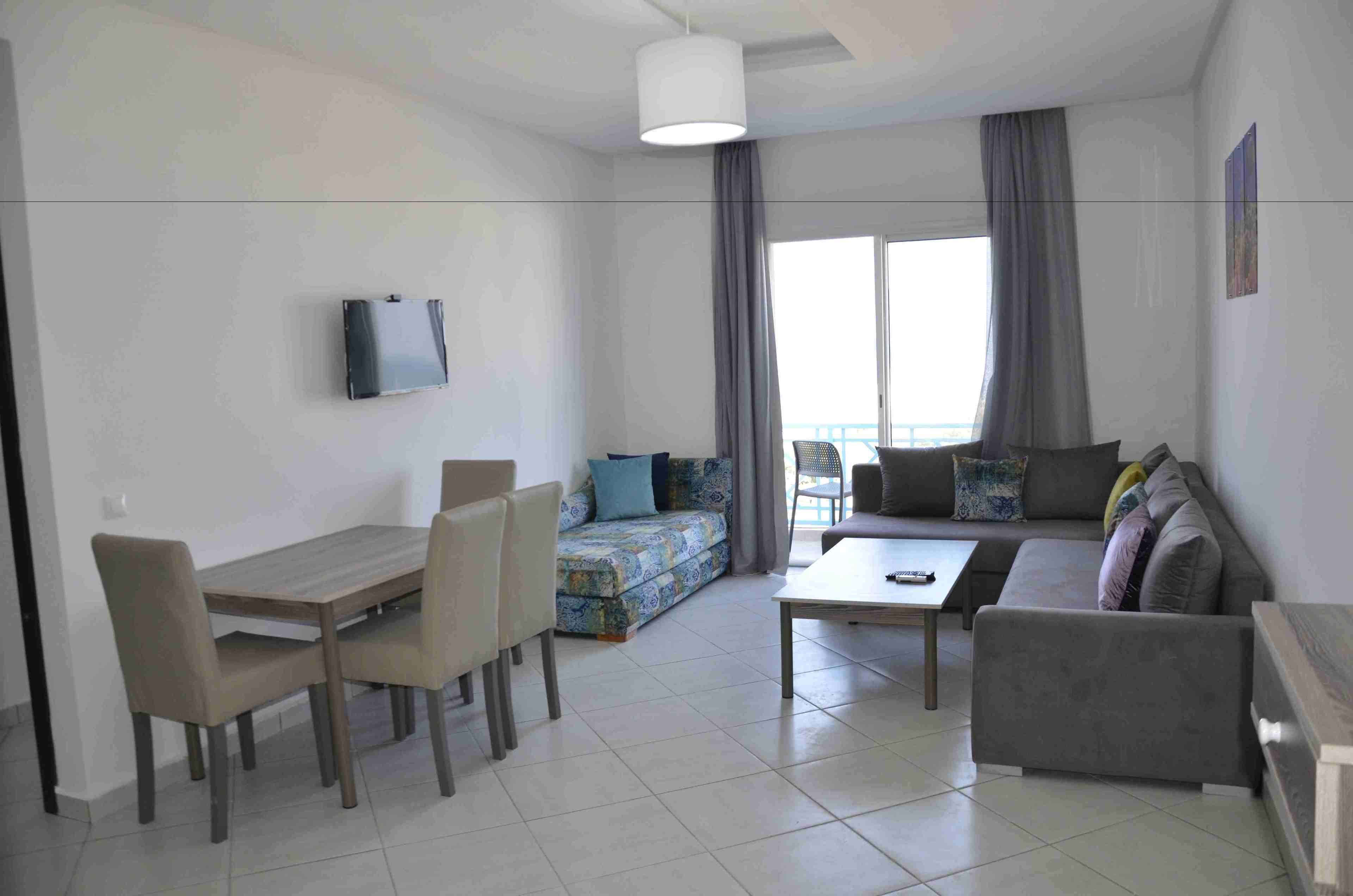 A modern living room with a dining area, a sofa, a coffee table, and a TV mounted on the wall.