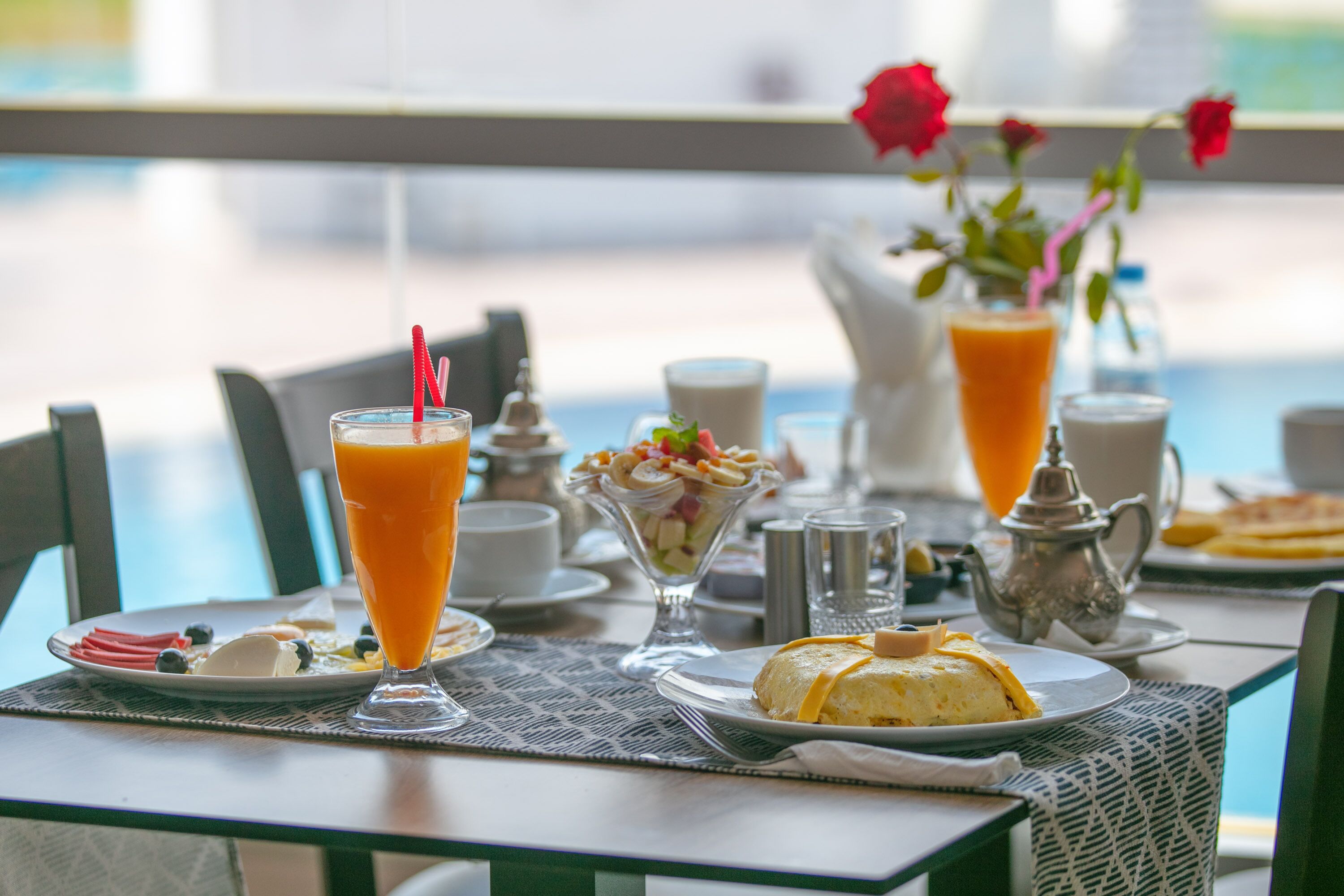Una tavola imbandita per la colazione, con diversi piatti tra cui un bicchiere di succo d'arancia, un'insalata di frutta e un dolce.