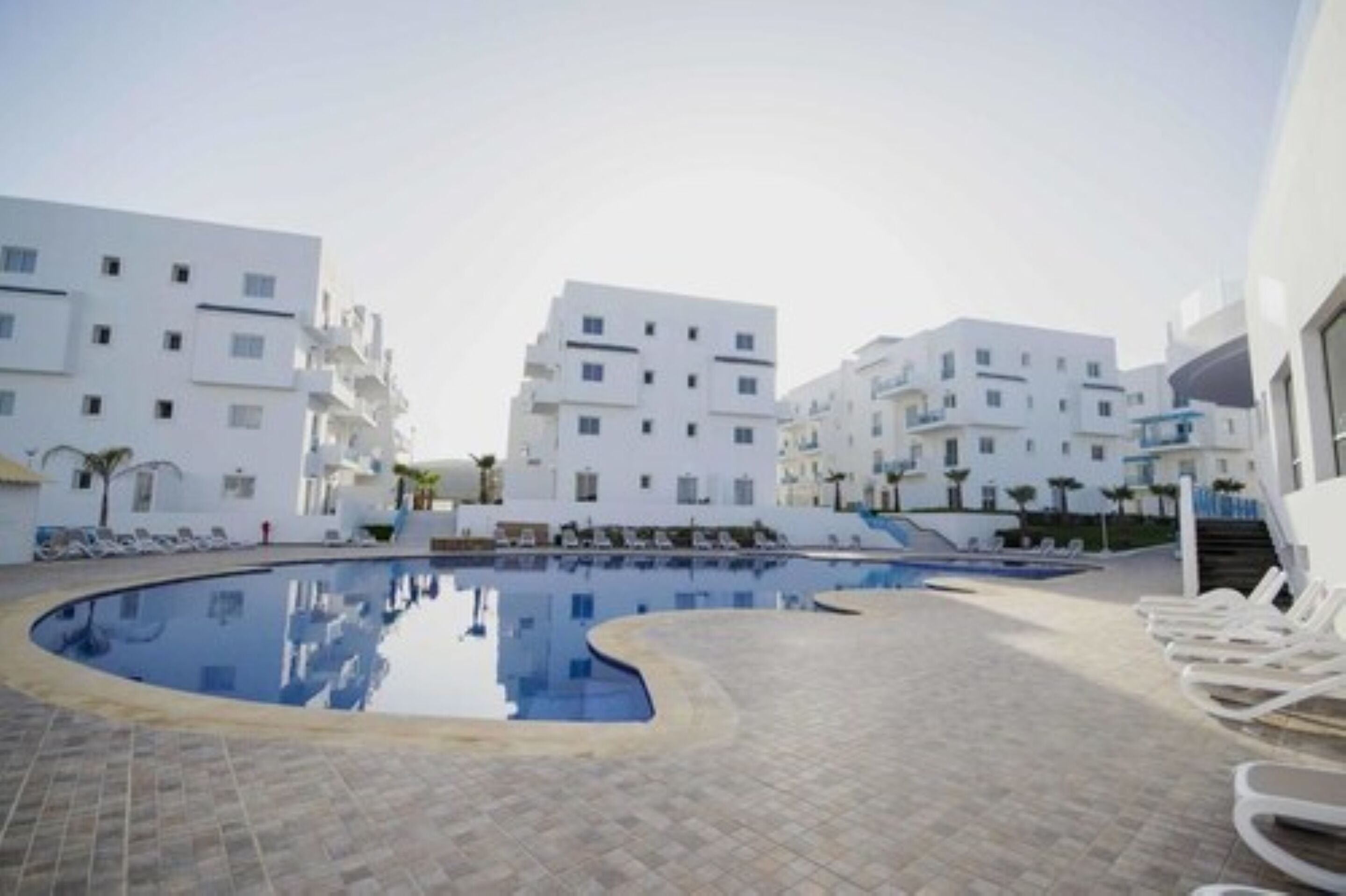 A modern hotel with a swimming pool surrounded by white buildings.