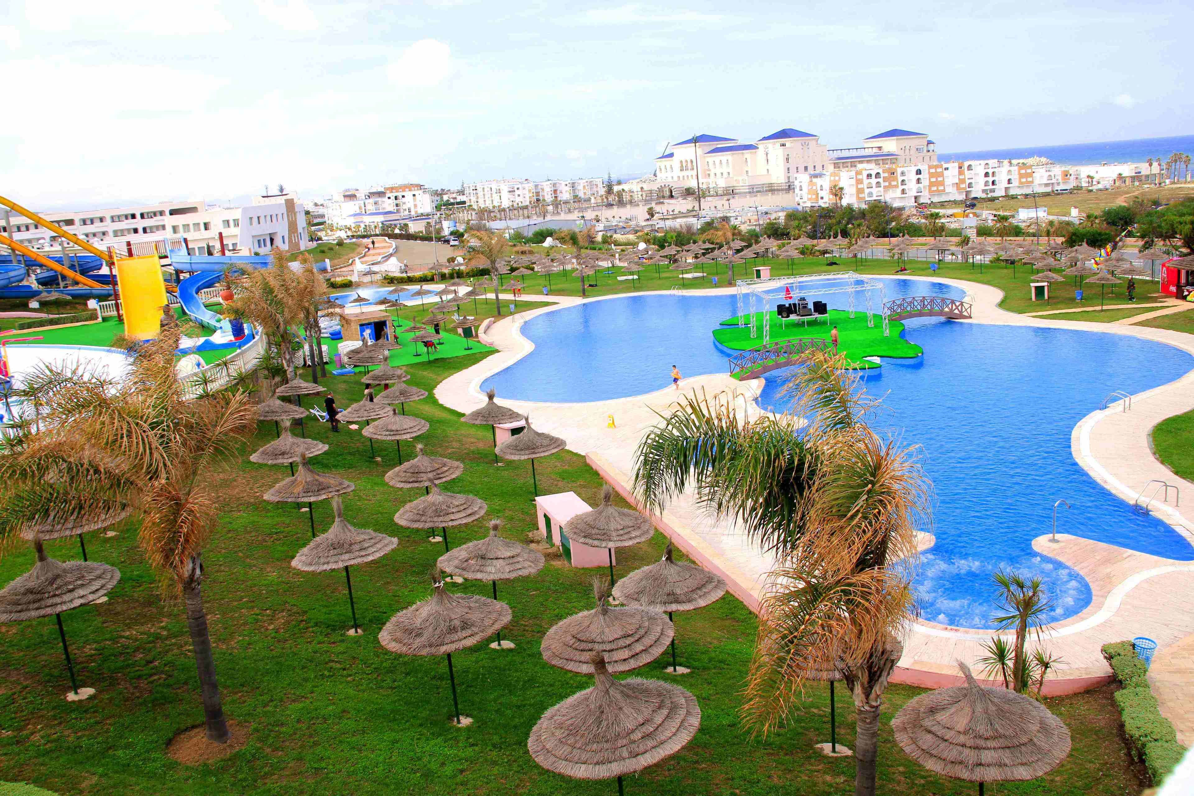 A large swimming pool with a boat, palm trees, and a water slide.
