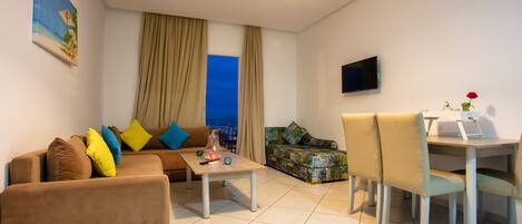 A modern living room with a sofa, a coffee table, a patterned sofa, and a dining area with chairs.