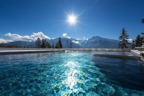 A clear blue pool with a mountain backdrop and a bright sun. - NIDUM - Casual Luxury Hotel (Telfs)