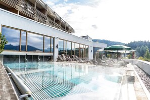 A modern hotel pool area with a clear view of mountains, lounge chairs, and umbrellas. - NIDUM - Casual Luxury Hotel (Telfs)
