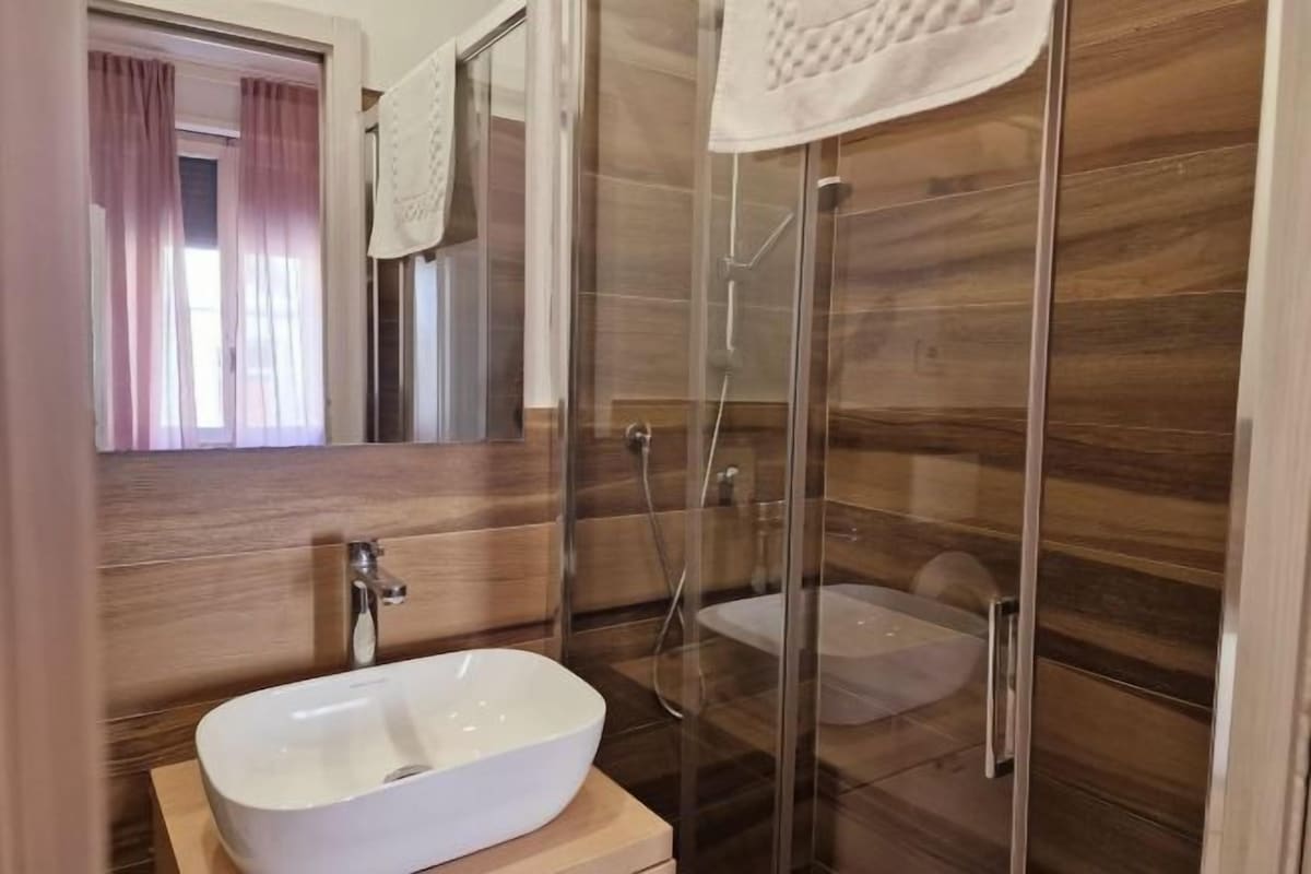 A modern bathroom with a glass-enclosed shower, a white sink, and wooden paneling.