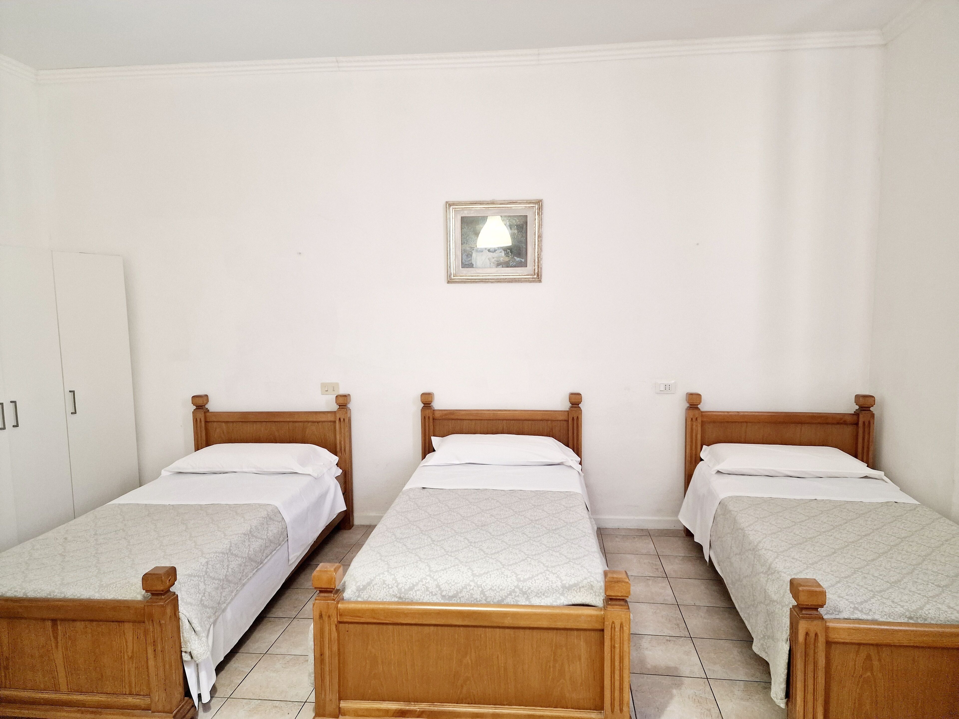 A room with three wooden beds, white walls, and a framed picture on the wall.
