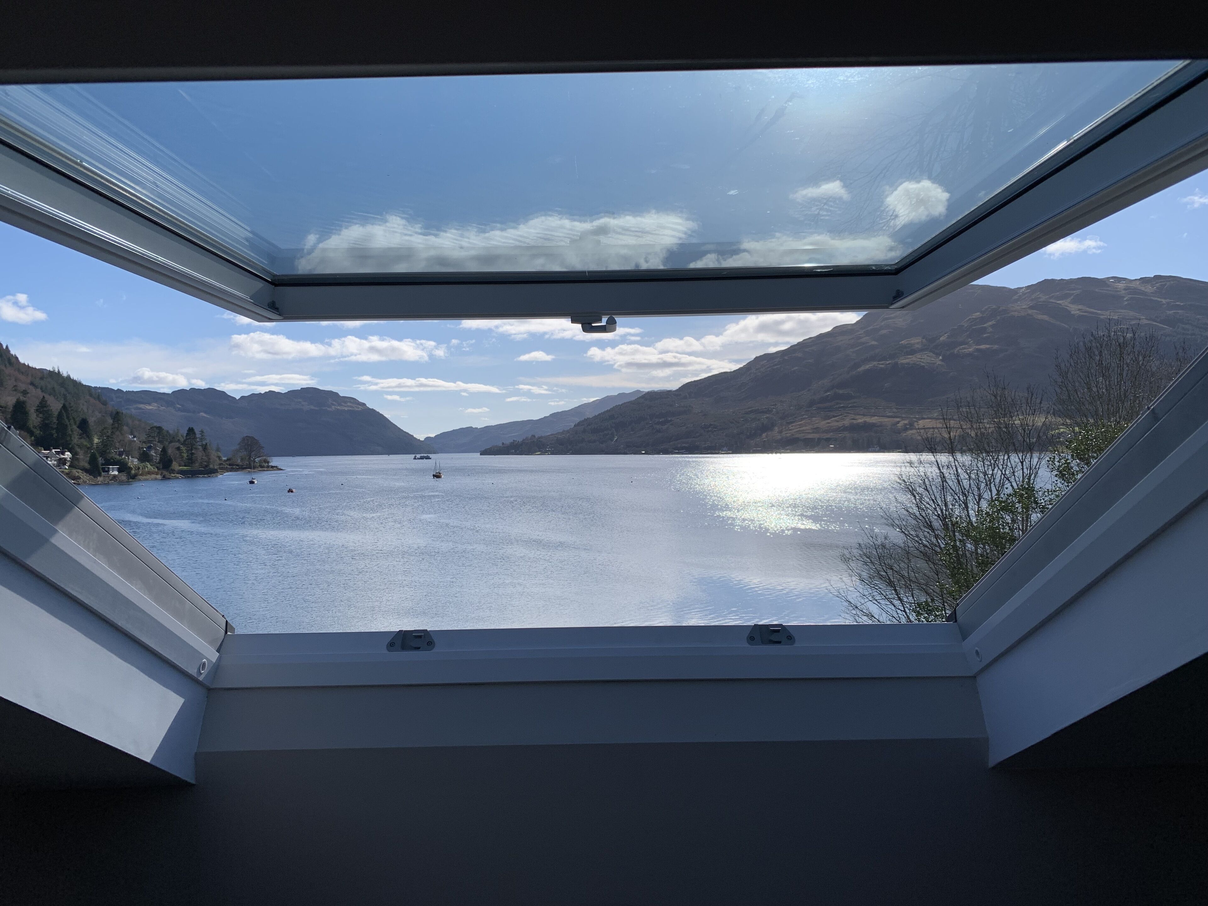 A view through a skylight of a lake with mountains in the background.