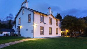 A two-story house with a well-maintained lawn and a pathway leading to the entrance. - The Shore House (Cairndow)