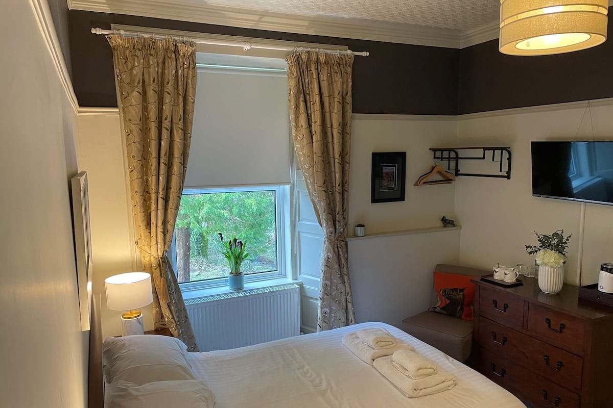 A hotel room with a bed, a dresser, a TV, and a window with curtains.