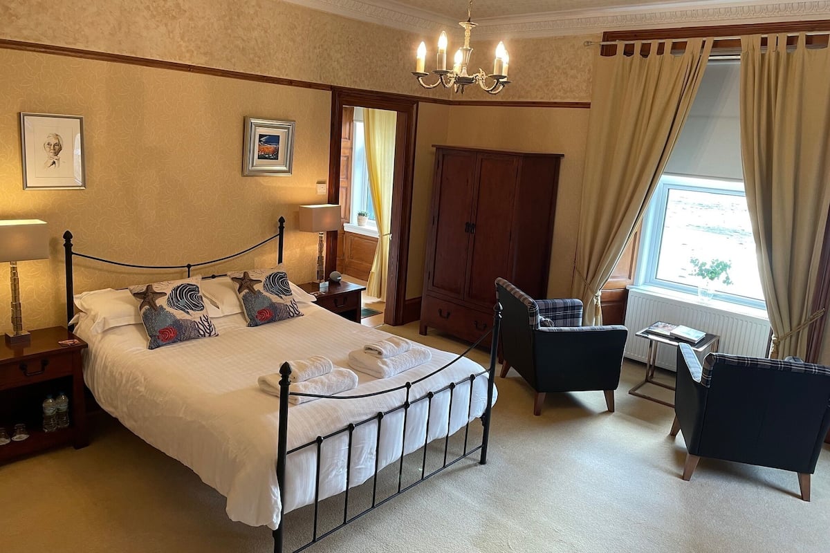 A hotel room with a large bed, a desk, a chair, a wardrobe, and a window with curtains.
