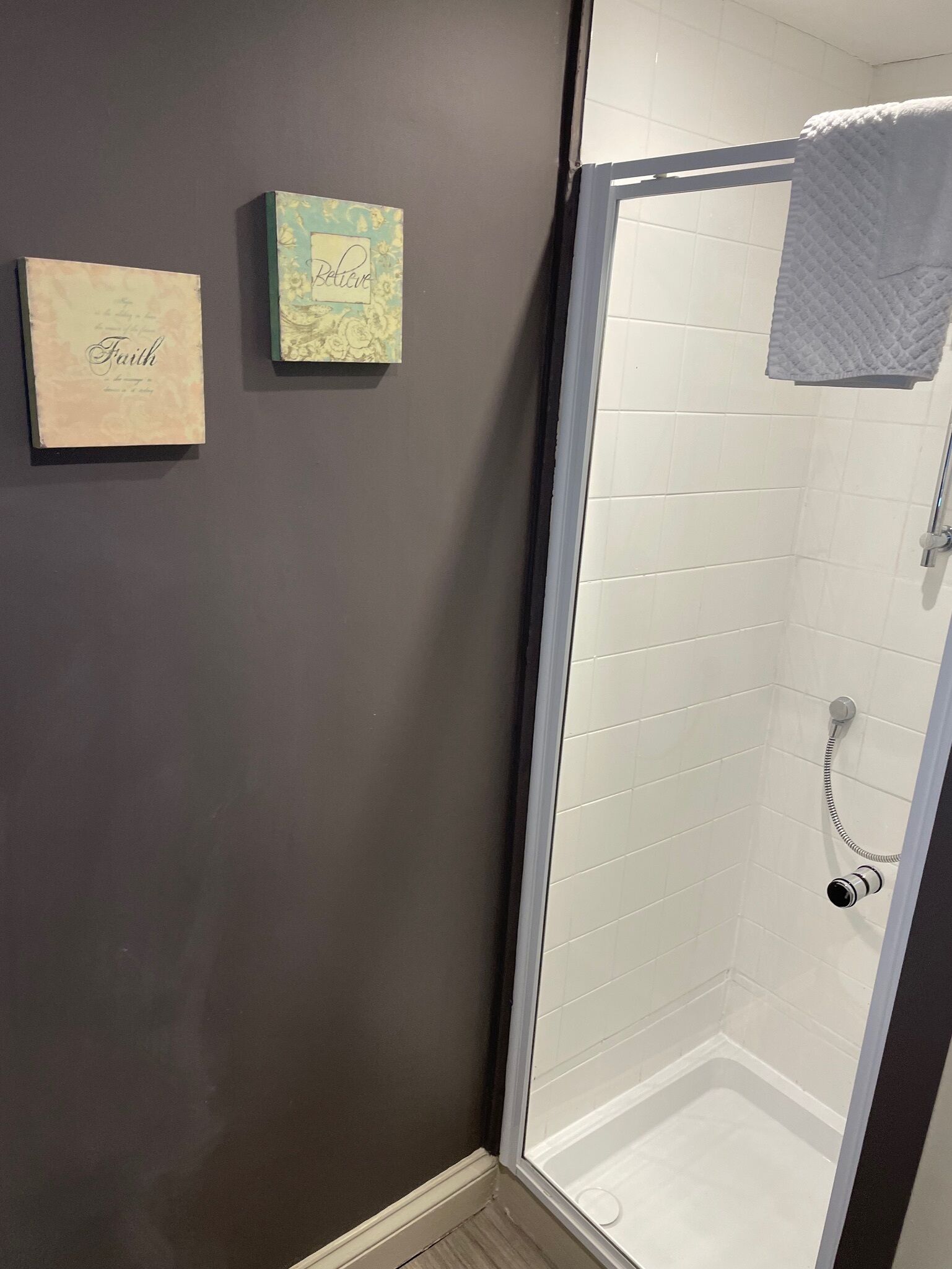 A shower area with a glass door, white tiled walls, and a dark gray wall.