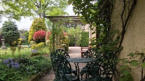 A garden patio with a table and chairs, surrounded by lush greenery and flowering plants. - Coombe House (Cheltenham)