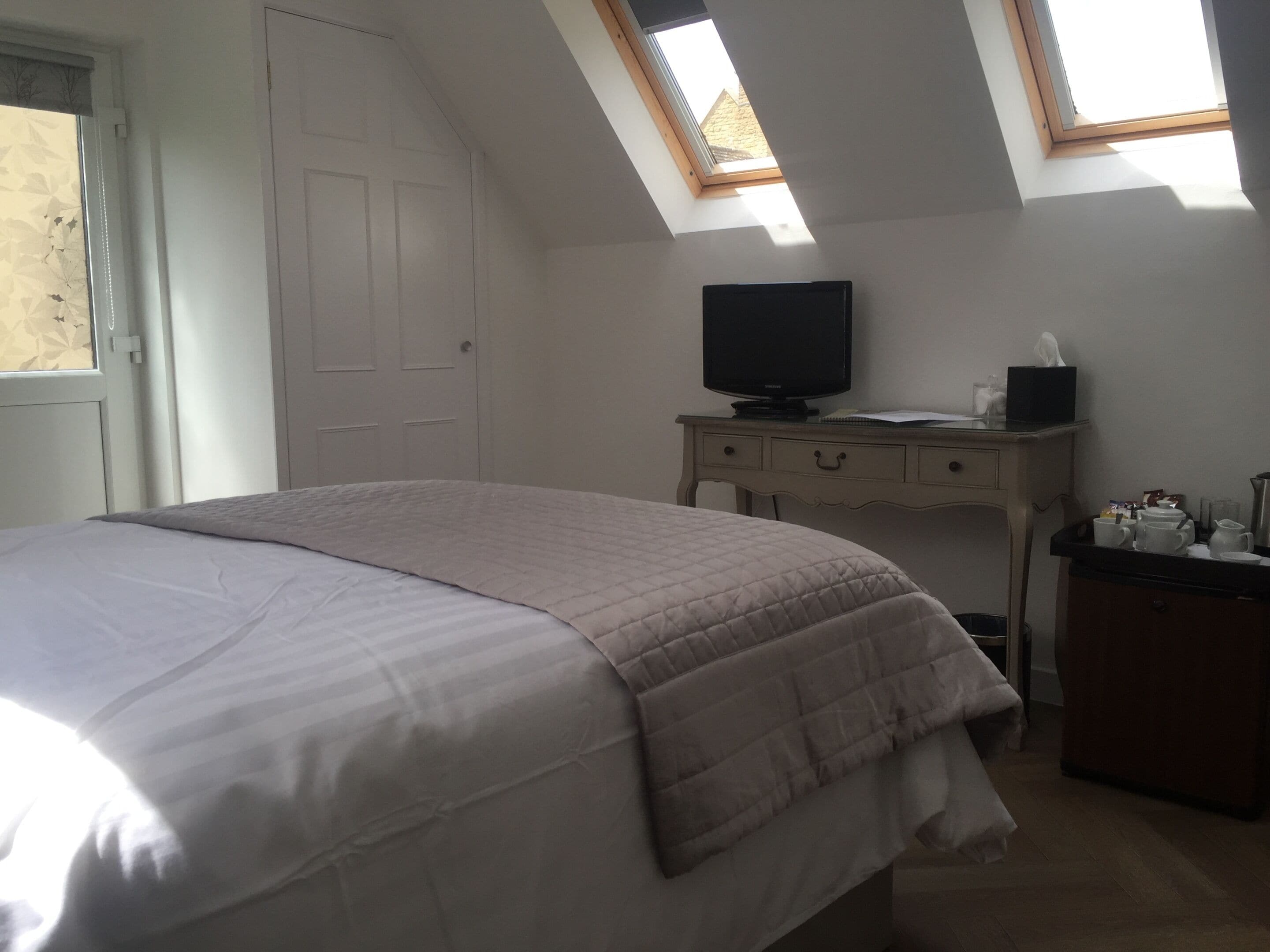 A bedroom with a bed, a desk with a television, and a window with a view of the outside.