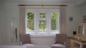 A bedroom with a bed, two armchairs, a dresser, and a window with curtains. - Coombe House (Cheltenham)