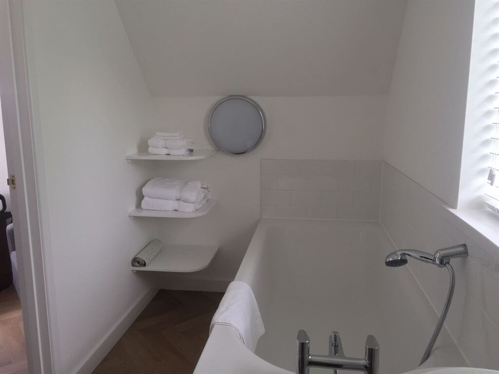 A small, white bathroom with a bathtub, a toilet, and a shelf with folded towels.