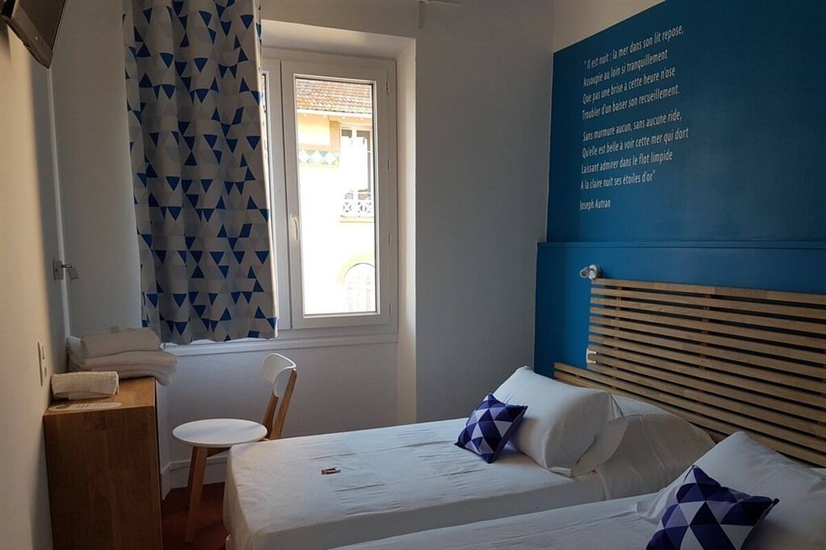Un dormitorio con dos camas, cabeceros de madera, una ventana con cortina geométrica y una pared con una cita.
