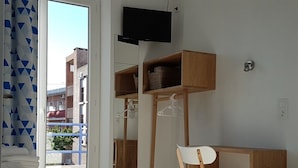 Un dormitorio con cama, escritorio y silla. Hay un televisor montado en la pared y una ventana con vistas a edificios.