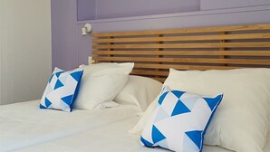 Una cama con cabecera de madera, dos almohadas con estampado geométrico y una pared con una placa que dice "William Shakespeare".