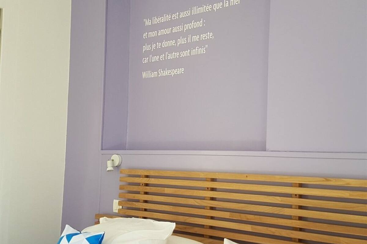 Un dormitorio con cabecera de madera, una cama con almohadas blancas y azules, y una pared con una cita en francés.