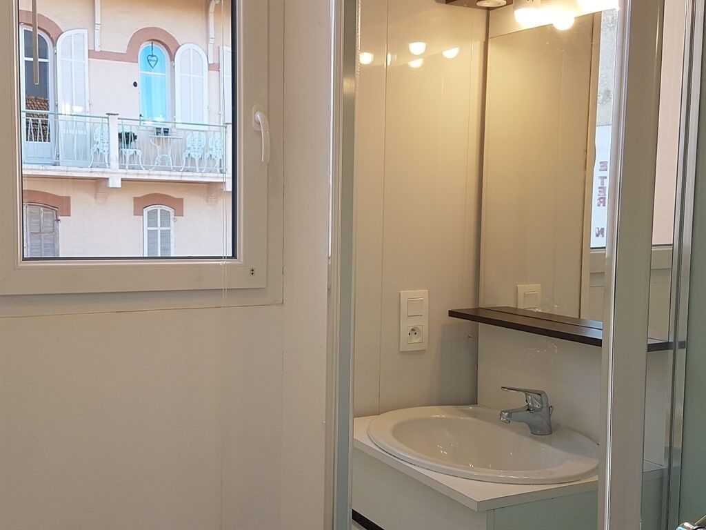 Un bany amb un lavabo blanc, un mirall i una finestra amb vista a un balcó amb mobles d'exterior.