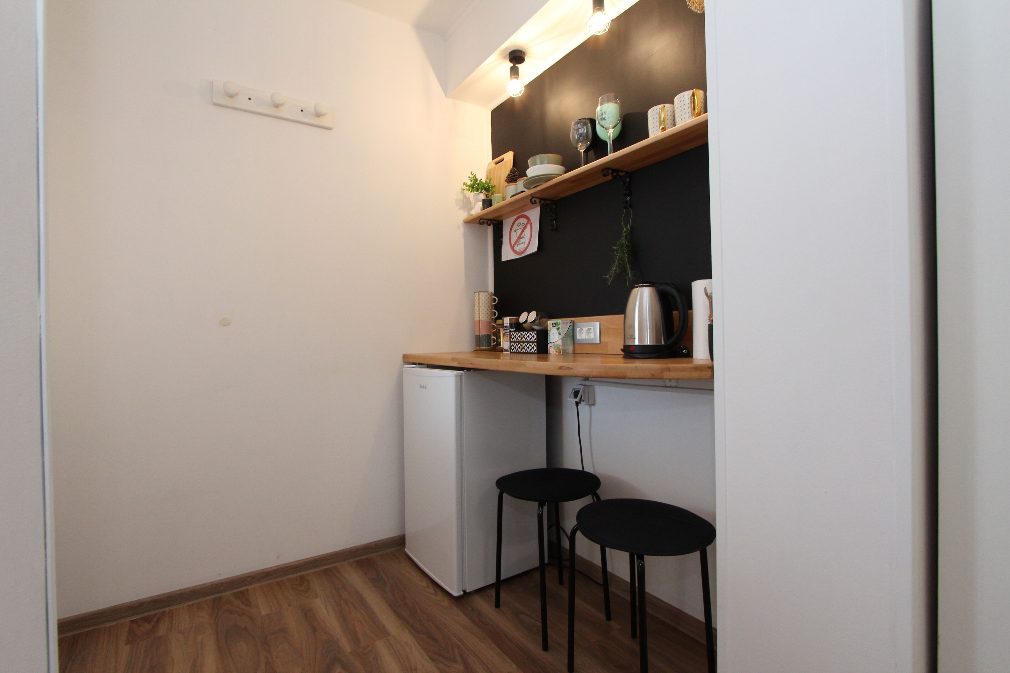 Una cucina compatta con un frigorifero bianco, due sgabelli neri e un piano di lavoro in legno con diversi oggetti da cucina.