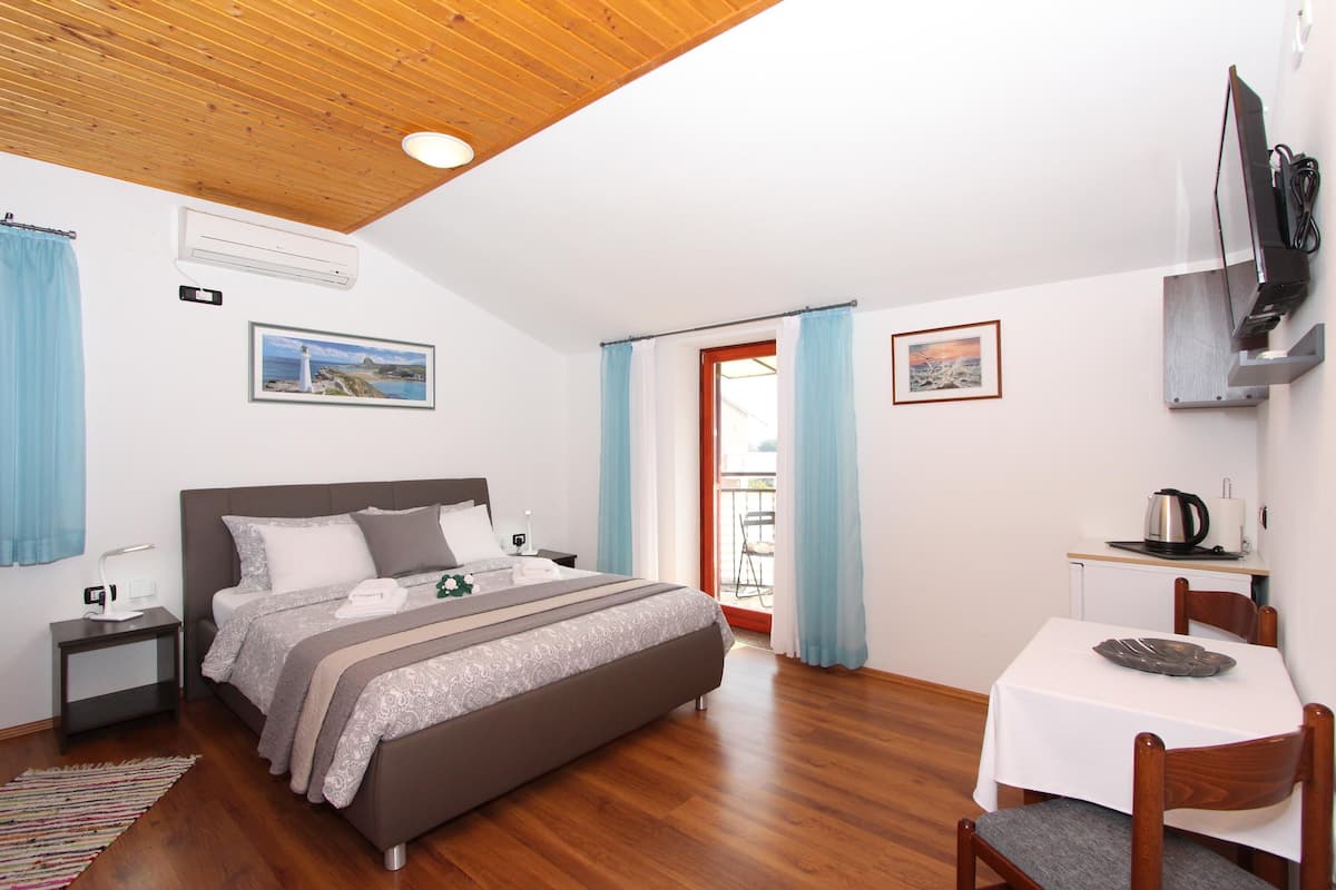 A bedroom with a bed, bedside tables, a desk with a chair, a television, and a window with curtains.