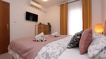 A hotel room with a bed, a TV mounted on the wall, an air conditioning unit, and a window with curtains.