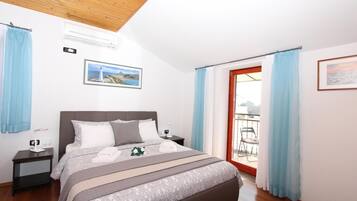 A bedroom with a bed, nightstands, an air conditioner, a picture on the wall, and a view through a door.