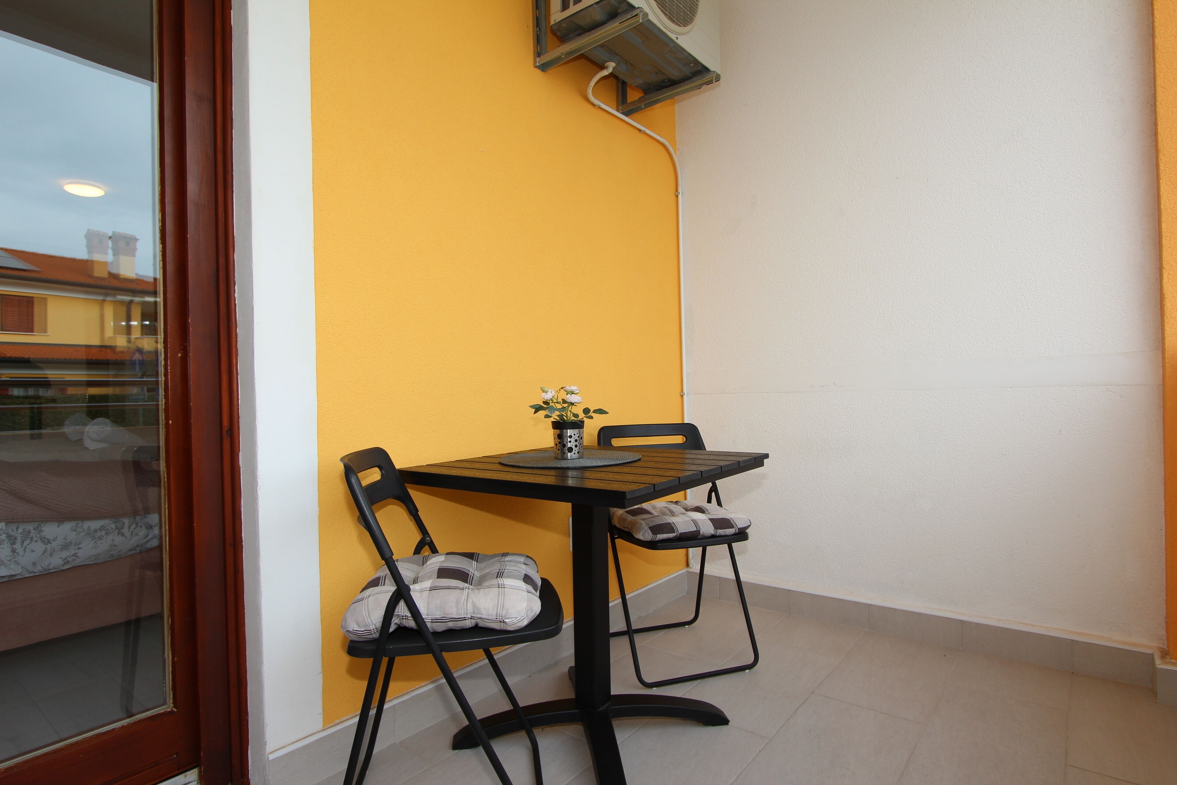 A small dining area with a table and two chairs, a window with a view of buildings, and a wall with a yellow accent.