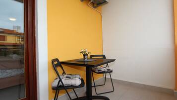 A small dining area with a table and two chairs, a window with a view of buildings, and a wall with a yellow accent.
