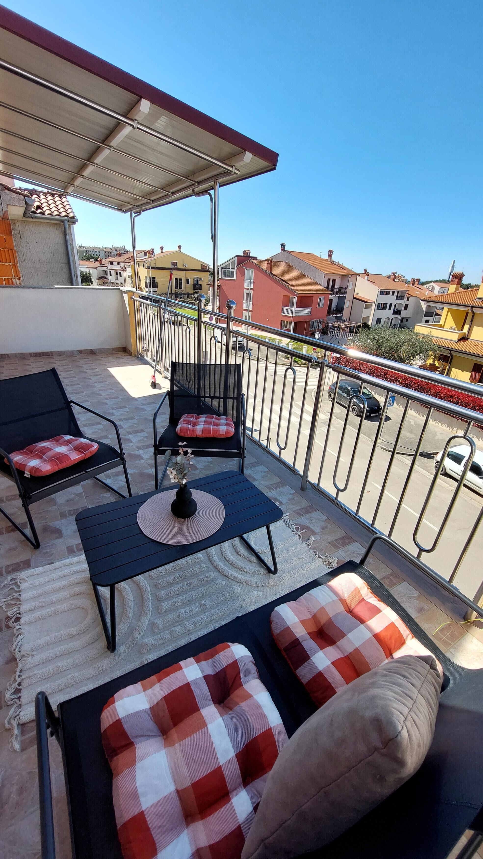 Un balcone con due sedie nere, un tavolino e un tappeto di vimini.