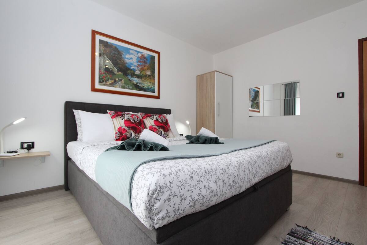A bedroom with a bed, a nightstand, a wardrobe, a mirror, and a painting on the wall.