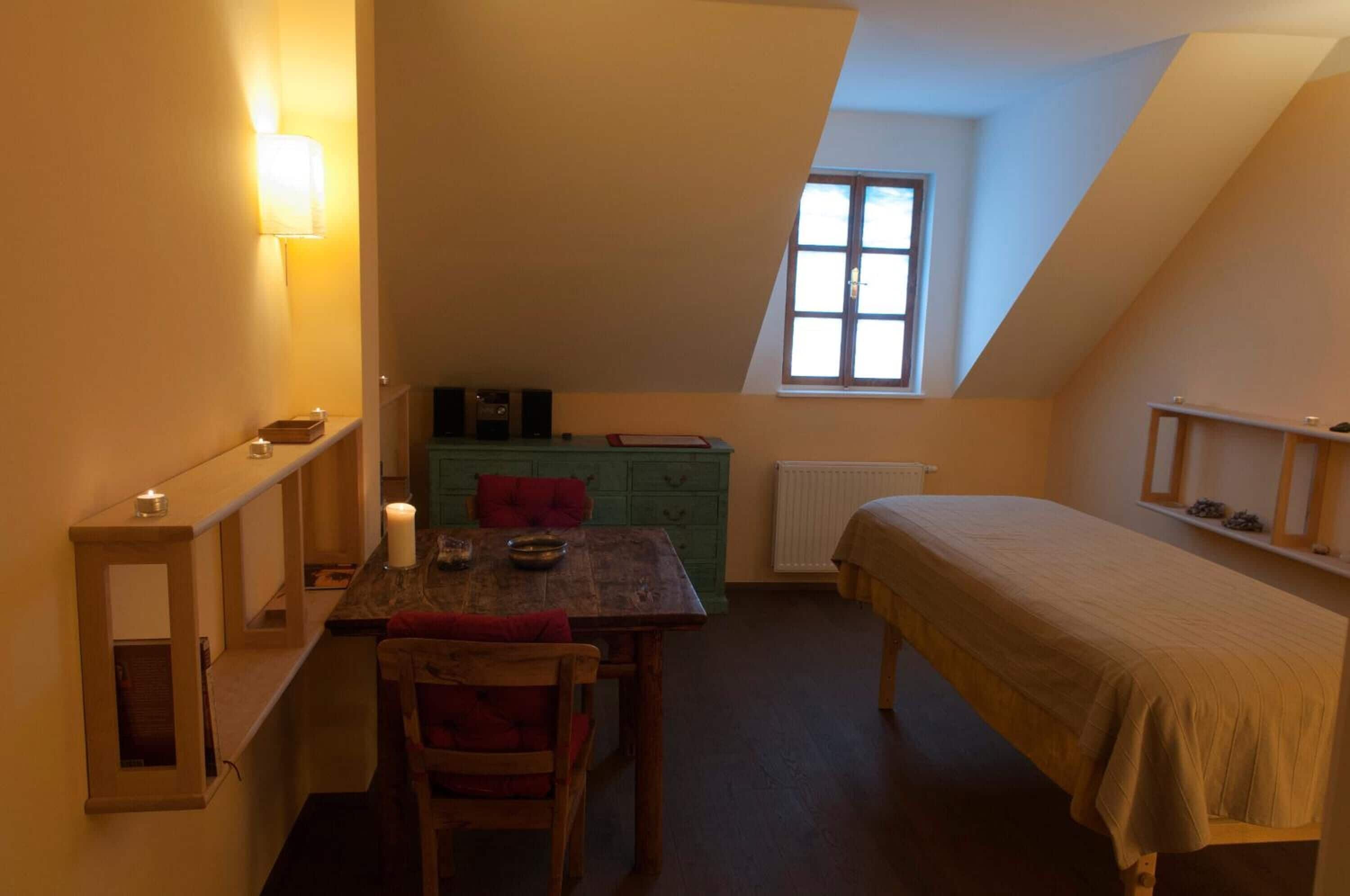 Una habitación pequeña y acogedora con una mesa de madera, una silla, una cama, un ventanal y un radiador.