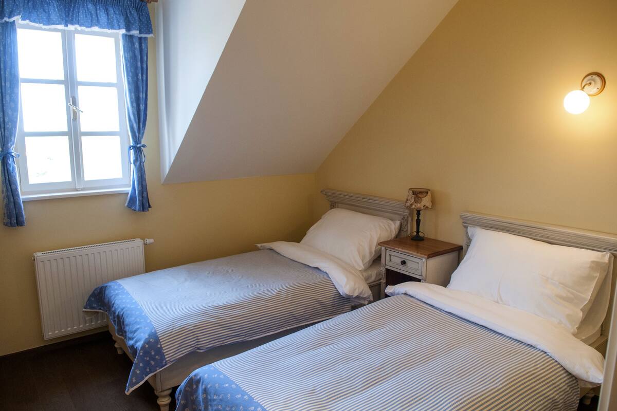 Ein Schlafzimmer mit zwei Betten, einem Fenster mit Vorhängen, einem Nachttisch mit Lampe und einer Heizung.