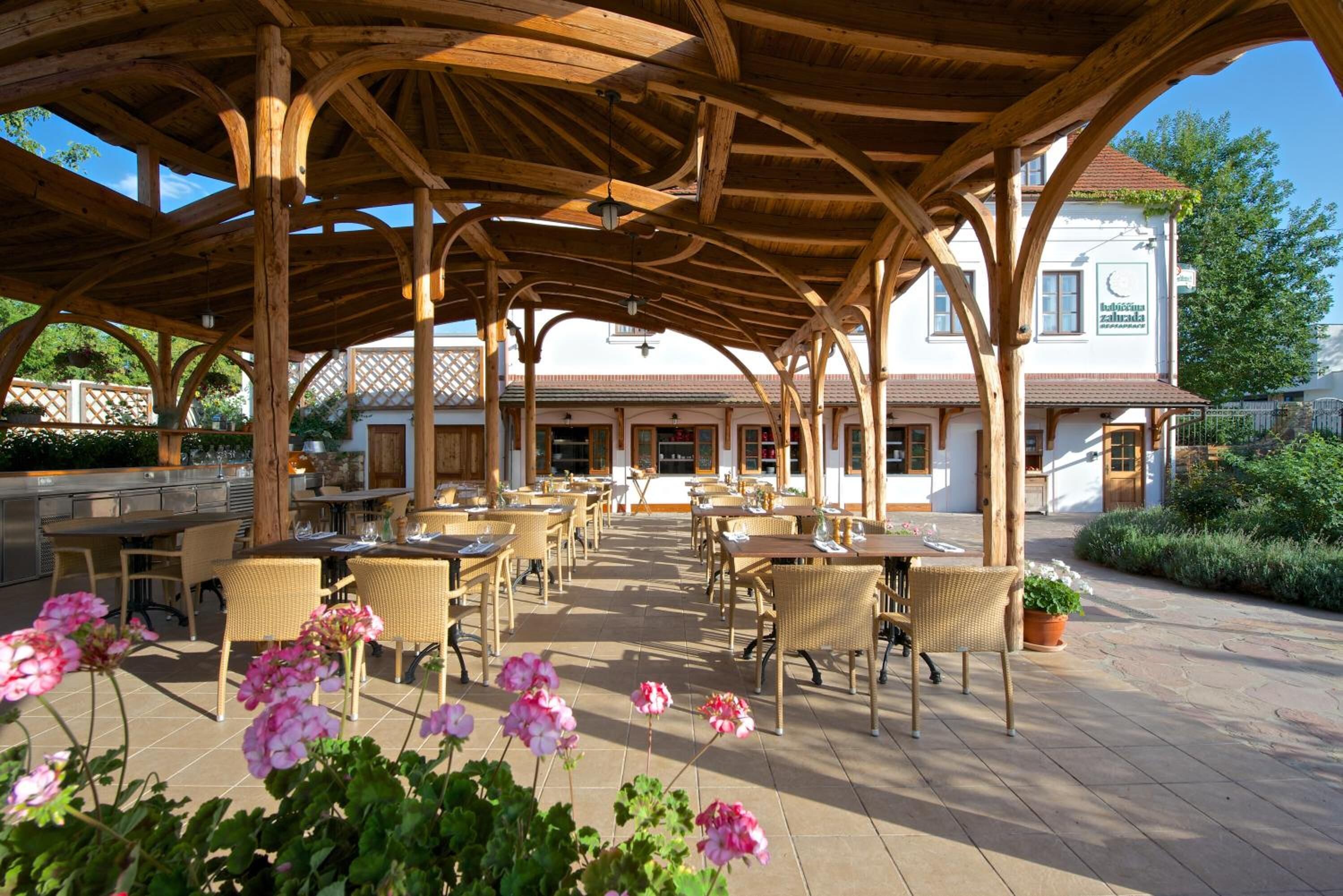 An outdoor patio with wooden beams, wicker furniture, and potted plants.