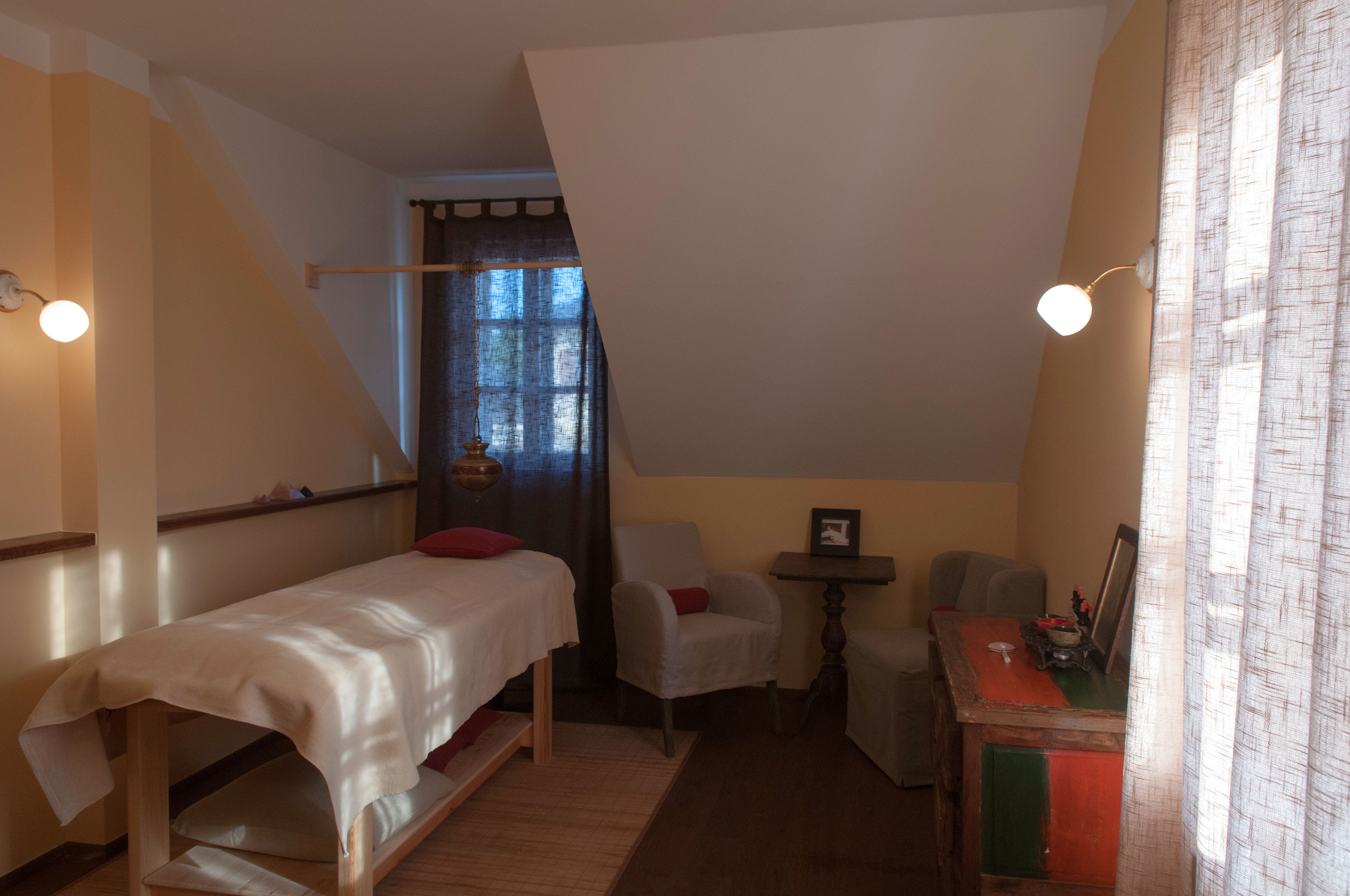 Una habitación pequeña y acogedora con una cama individual, una silla, una mesita y una ventana con cortinas.