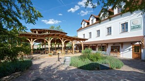 Ein traditioneller europäischer Innenhof mit einer Holz-Pergola, Steinböden und einem weißen Gebäude mit Hinweisschild für ein Restaurant.