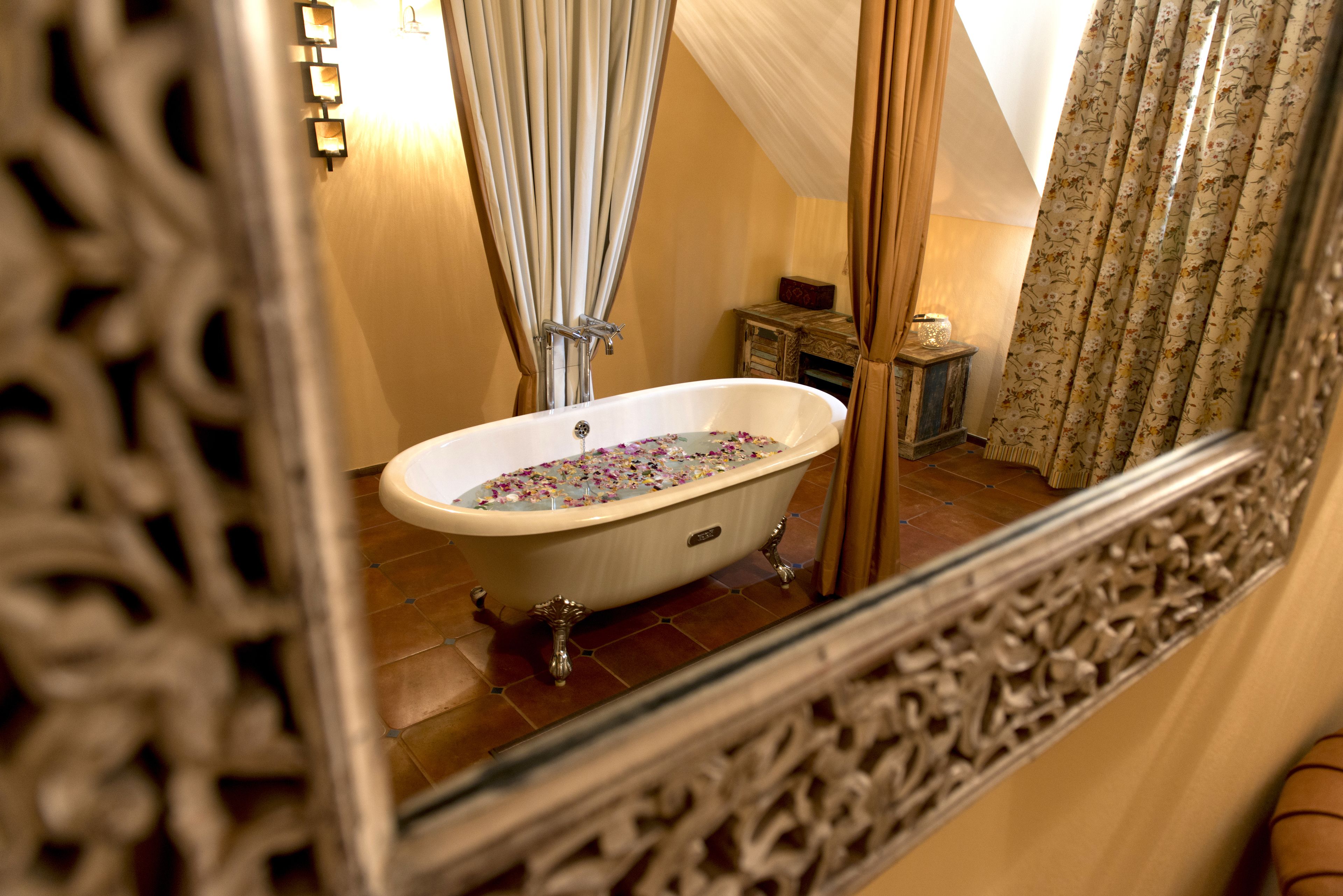 A bathroom with a freestanding bathtub, a small wooden cabinet, and a mirror with ornate detailing.