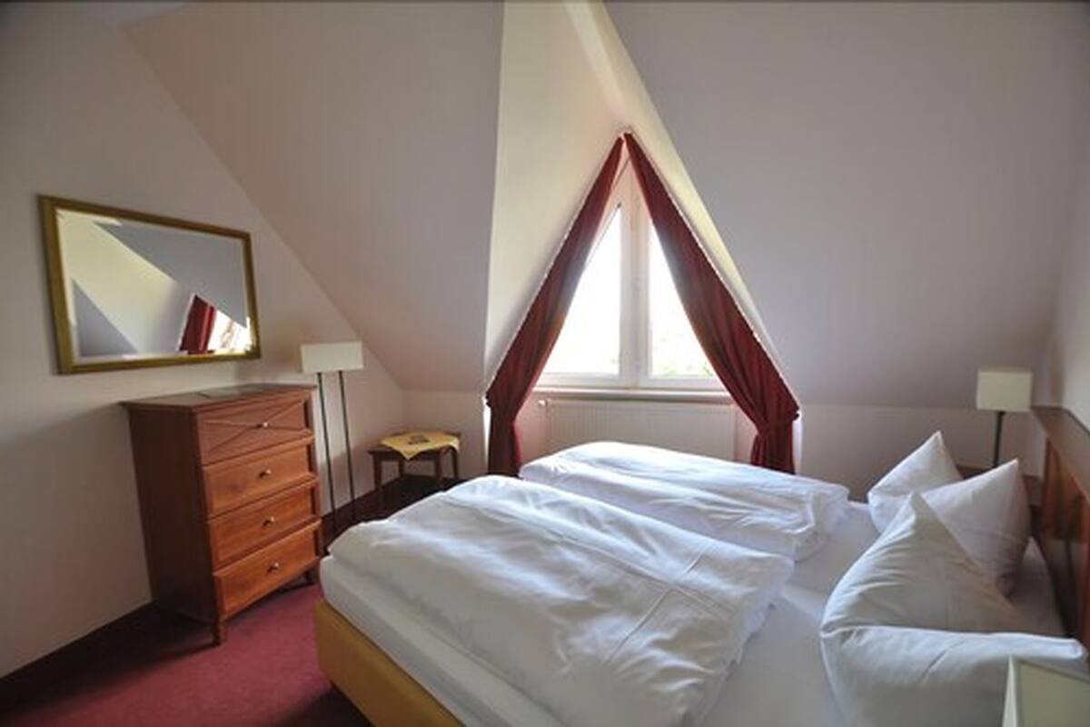 A bedroom with a bed, a dresser, a small table, a mirror, and a window with curtains.