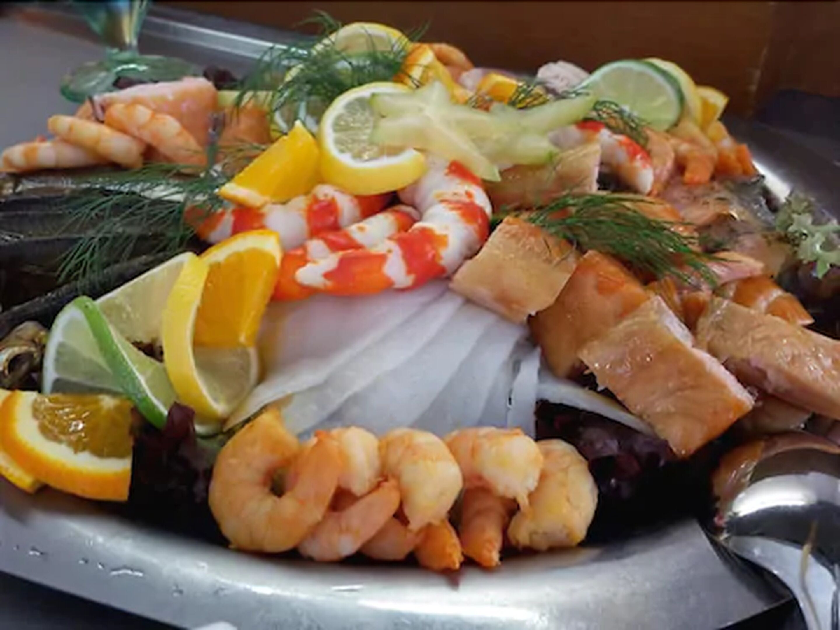 Una bandeja de mariscos con camarones, salmón y rodajas de limón.