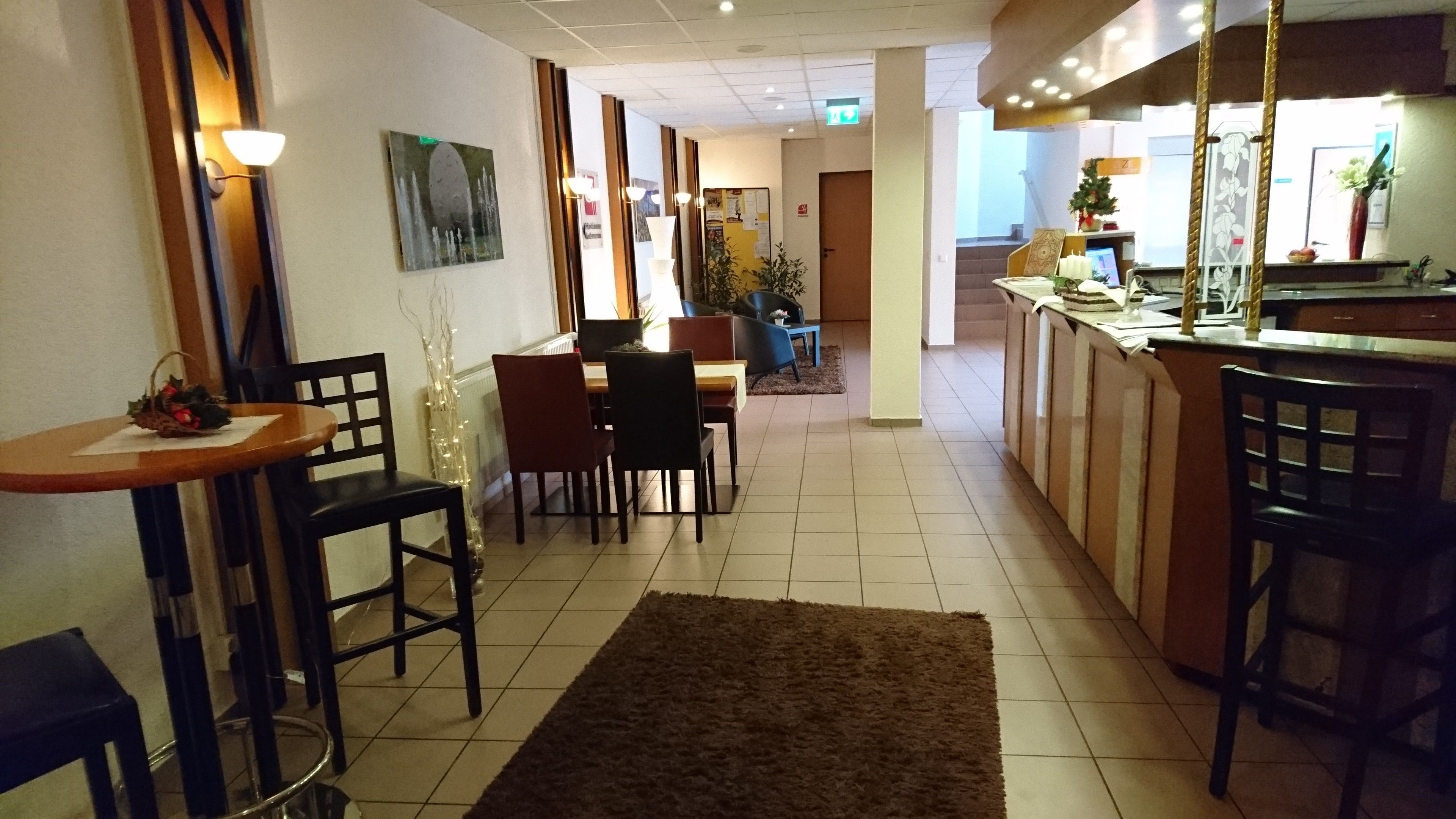 A restaurant with a bar area, wooden chairs, a brown rug, and a painting on the wall.