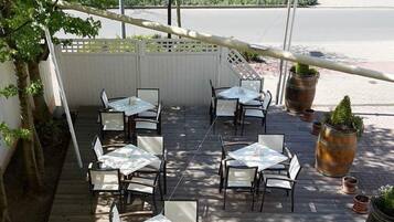 An outdoor patio with tables and chairs, surrounded by a wooden deck and potted plants.