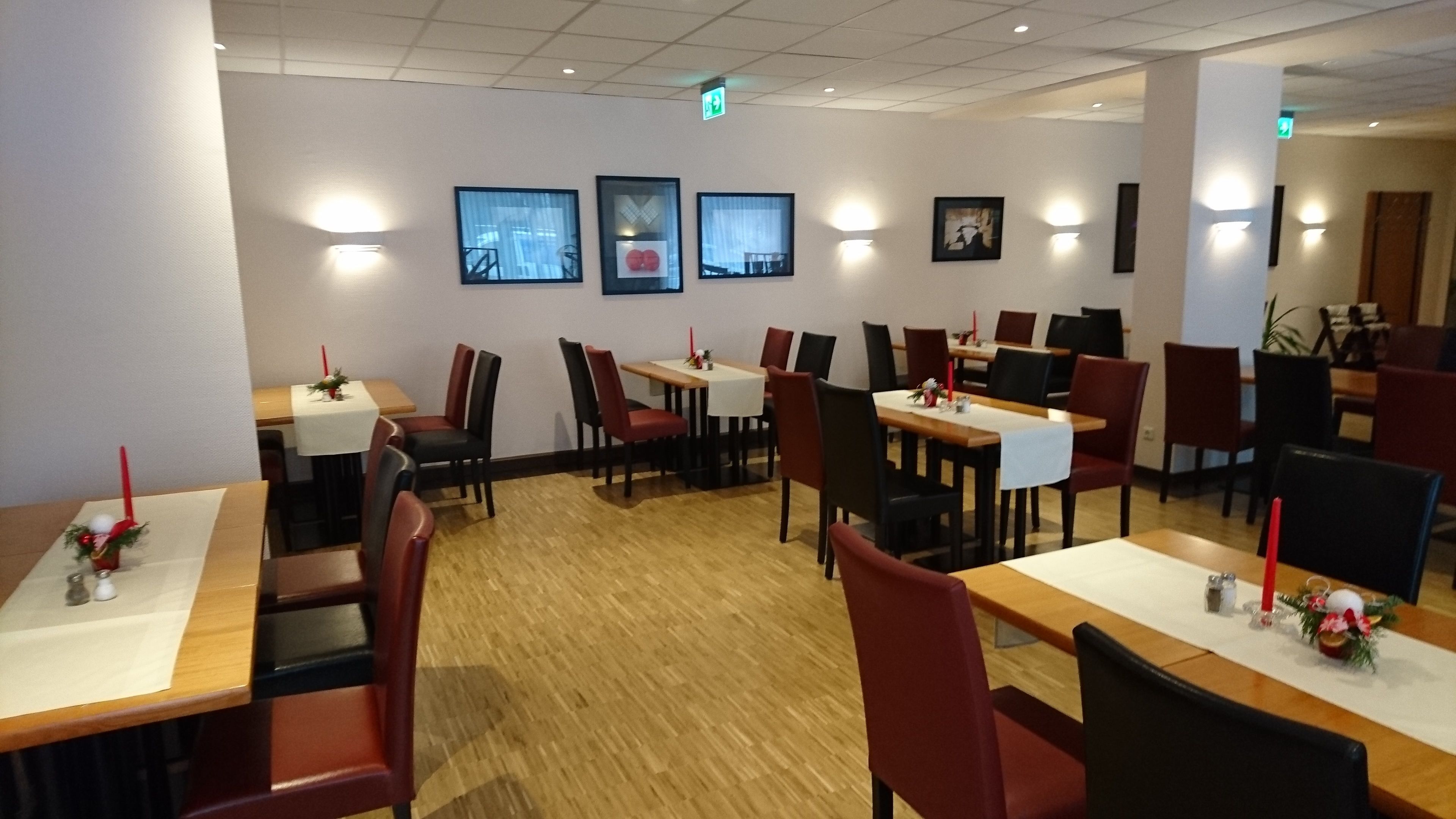 Ein Restaurant mit mehreren Tischen und Stühlen, Holzböden und gerahmten Bildern an den Wänden.